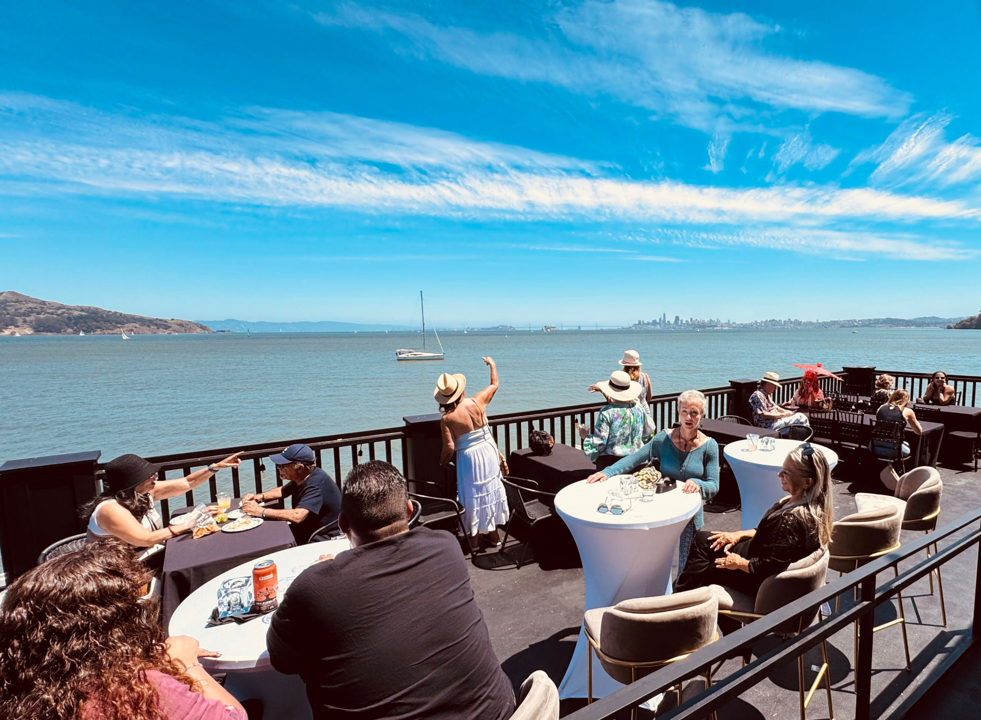 Guests at tables on ERIA's waterfront deck in Sausalito, sailboats on the bay and the San Francisco skyline in the distance
